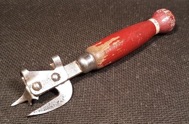 This can opener with a worn wooden red handle shows the wear and tear of years of use, a staple in households of the past